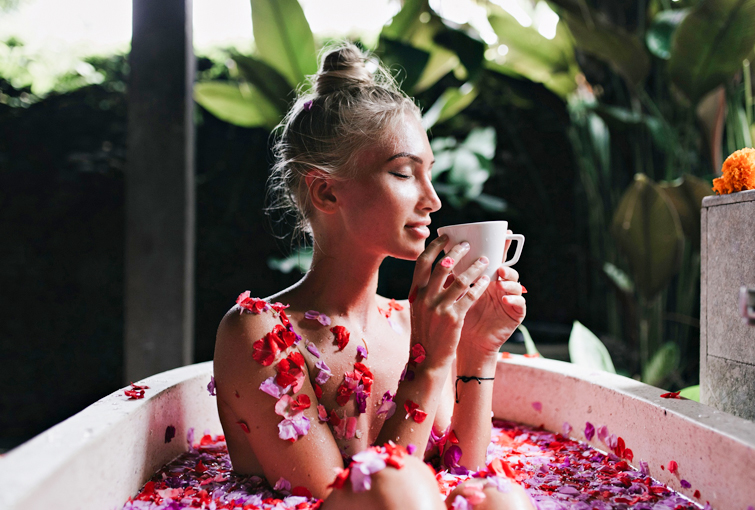 Flames Beauty Care & Bridal Studio, A woman relaxes in a flower-adorned bathtub, enjoying tea, at Flames Beauty Care & Bridal Studio's Moroccan & Ice Bath.